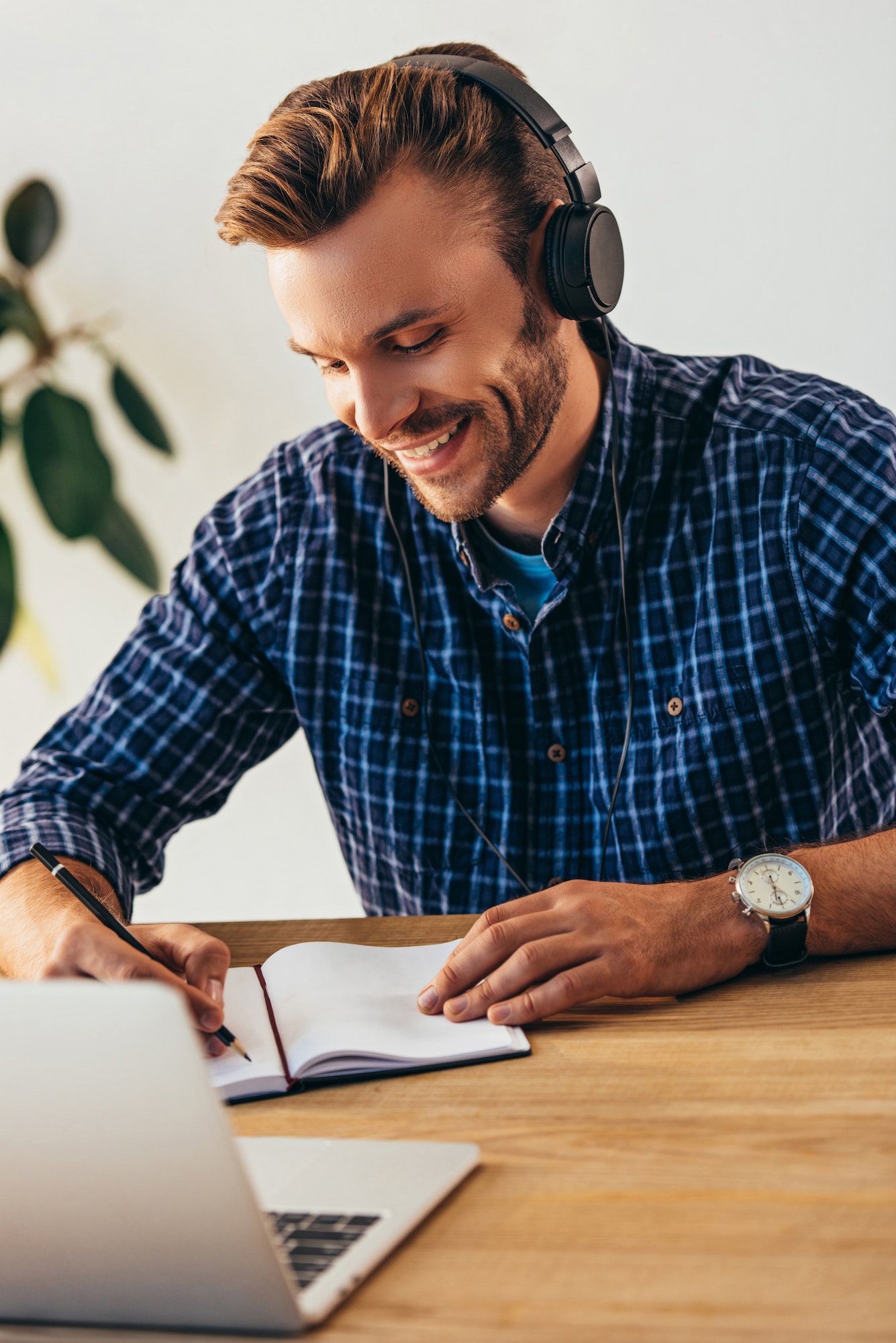 portrait of smiling man in headphones making notes while taking part in webinar at tabletop with